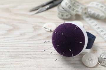 Blue pincushion with pins and other sewing tools on light wooden table. Space for text