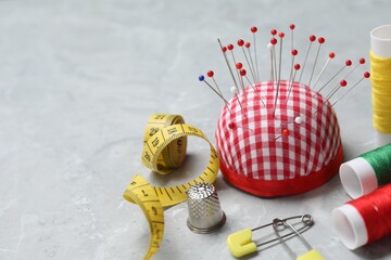 Checkered pincushion with pins and other sewing tools on grey table