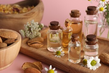 Aromatherapy. Different essential oils, flowers and almonds on pink background