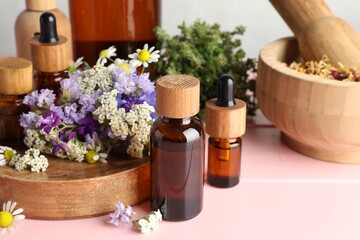 Aromatherapy. Different essential oils, mortar, pestle and flowers on pink wooden table
