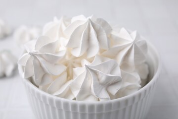 Delicious meringue cookies in bowl on white table, closeup