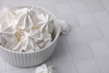 Tasty meringue cookies in bowl on white tiled table. Space for text