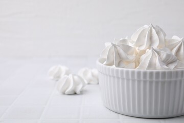 Delicious meringue cookies in bowl on white tiled table, closeup. Space for text