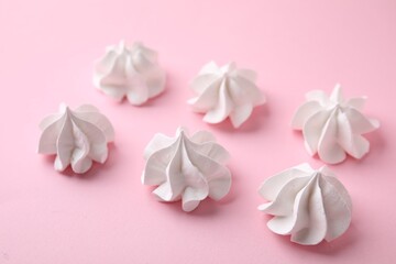 Many tasty meringue cookies on pink background