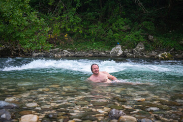 Adventurous man with long hair swimming in a scenic mountain river surrounded by rocks and trees