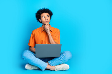 Full length photo of doubtful unsure guy dressed orange shirt working modern device emtpy space isolated blue color background