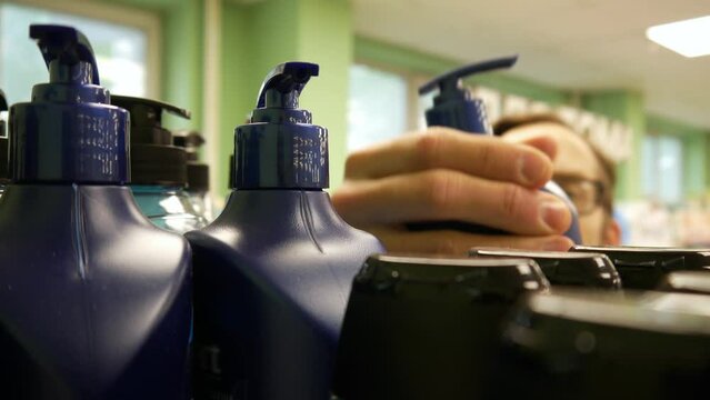 Close-up of nice plastic bottles of shower gel or shampoo in a supermarket and a male buyer choosing one