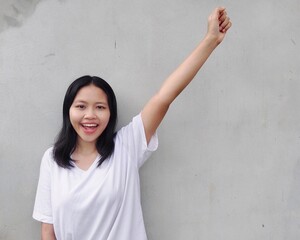 Portrait of Happy, excited, Joyful, Surprised, shocked Asian woman  raising her arm up Smiling and screaming for success, standing against grey background