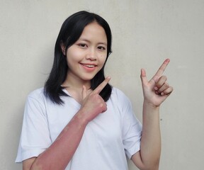 Image of portrait Waist up happy young woman standing isolated, smiling while pointing finger right, recommending product, Looking camera pointing, over grey background