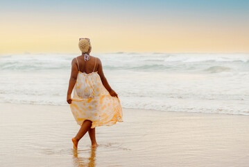 young latin girl dressed in a summer dress walking alone by the sea shore