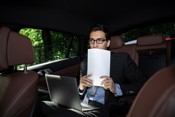 Depressed businessman sitting on backseat of his luxury car and feeling bad after overloaded work...