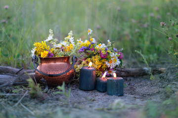 Copper witch cauldron with flowers, magic candles on meadow, abstract natural background. herb...