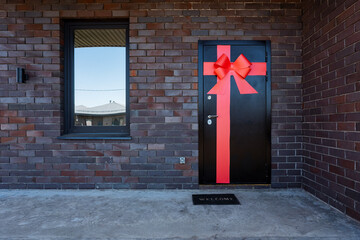 A modern brick house entrance with a front door adorned with a red bow is perfect for welcoming...
