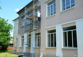A painter climbs a ladder onto scaffolding to paint the wall of a house.