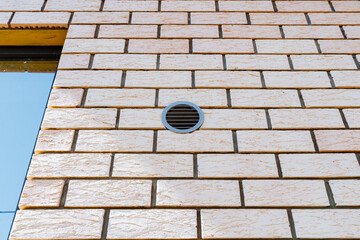 Detailed urban architectural design featuring an exterior brick wall with a round vent illuminated by natural light, adding texture and depth to the building facade