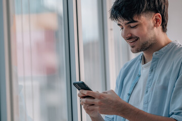 young man with mobile phone indoors next to the window