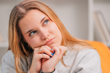 portrait of young blue eyed blonde woman or student at home thinking