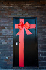 A black door with a red bow stands out against the brickwork, offering a fascinating symbol that...