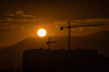 Sunset silhouette of construction cranes and buildings