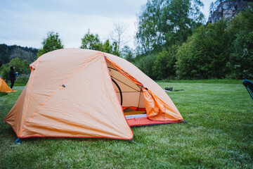 A serene outdoor spot hosts an orange camping tent surrounded by trees and grass, offering a...