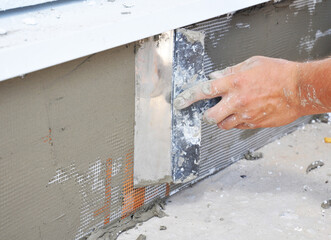 The builder applies plaster with a spatula to the reinforcing mesh  on top of a layer of rigid foam...
