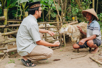 Serious Asian Muslim man discussing with cattleman to buy livestock goats for sacrifices. Eid Al...