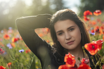 Naklejka premium Portrait of sadly smiling brunette girl with her hand in hair in red poppies field. Horizontally. 