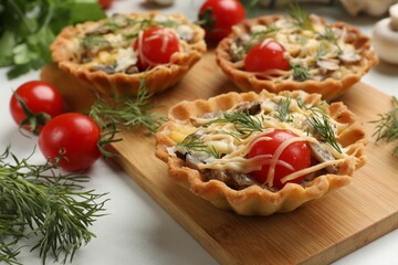 Tasty tartlets with cheese, tomatoes, mushrooms and dill on white table, closeup