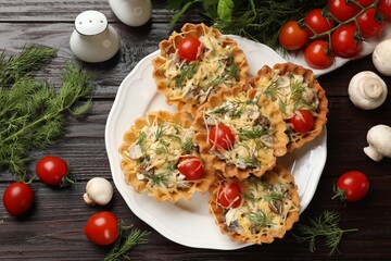 Tasty tartlets with cheese, tomatoes, mushrooms and dill among ingredients on wooden table, flat lay