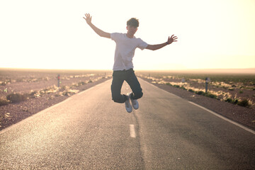 Young man jumping in the middle of lonely road. Employment horizon concept