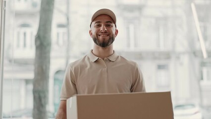 Portrait of a smiling delivery man in casual attire holding a cardboard box, standing confidently in an office setting.
