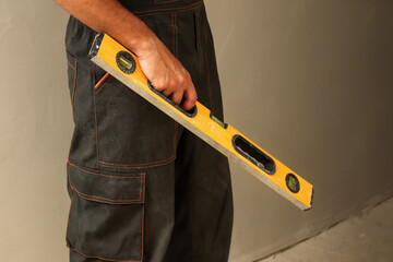 Close-up of man holding level tool, builder’s dirty hands, construction worker in overalls....