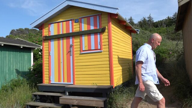 Tisvilde, Denmark A man walks past a colourful beach hut on the beach