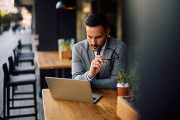 Male entrepreneur working on laptop while drinking coffee in café.