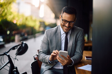 Happy businessman text messaging on cell phone in café.