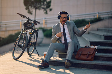 Happy businessman singing and having fun while listening music on headphones in city.