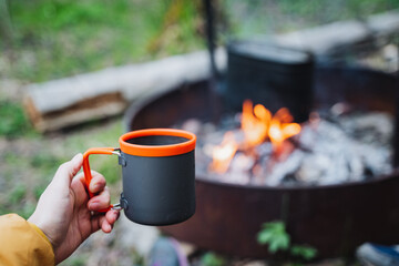 Person holds cup of coffee by fire pit with charcoal heat
