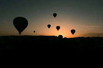 Hot air balloons silhouetted against the dawn sky in Cappadocia, creating a serene and captivating scene. The balloons float gracefully over the rugged landscape as the first light of day breaks.