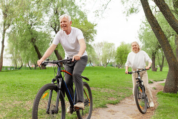 Obraz premium elderly senior couple rides bicycle in the park in the summer and smiles, old gray-haired man and woman are actively resting outdoors, old people practice cycling in forest