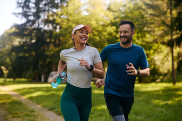 Cheerful athletic couple jogging through park. - Powered by Adobe