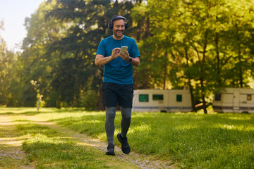 Happy athlete listening music on headphones while using smart phone during outdoor workout.