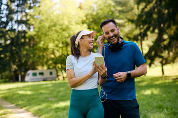 Happy athletic couple using smart phone while listening music over earphones in  park.