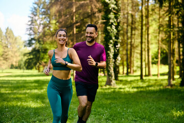 Happy couple of athletes running while exercising in nature.