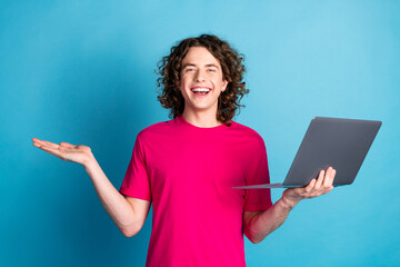 Portrait of nice young man arm hold laptop empty space wear pink t-shirt isolated on blue color...