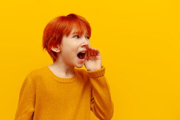 red-haired boy child shouts and announces information on a yellow isolated background, teenager...