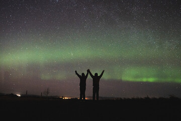 Two people celebrating under the northern lights in Iceland