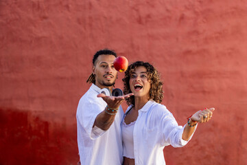 Couple in white levitates an apple, red background