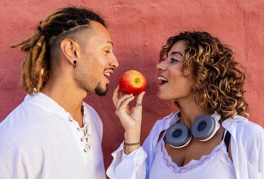 Young couple sharing an apple against a colorful background
