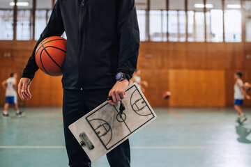 Cropped picture of basketball coach holding ball and clipboard on court - Powered by Adobe