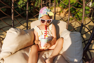 Funny cute girl drinks a cocktail on summer vacation. The child has fun on the beach. Cute baby in...
